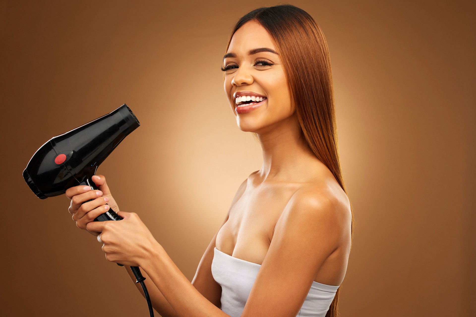 Hair, hairdryer and smile portrait of woman in studio for growth, color or healthy texture. Aesthetic female hands with heat for haircare, self care and hairdresser or beauty salon brown background